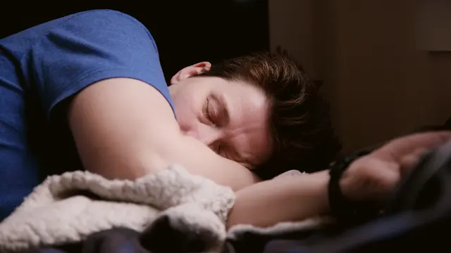 A man asleep on his side under a soft blanket.