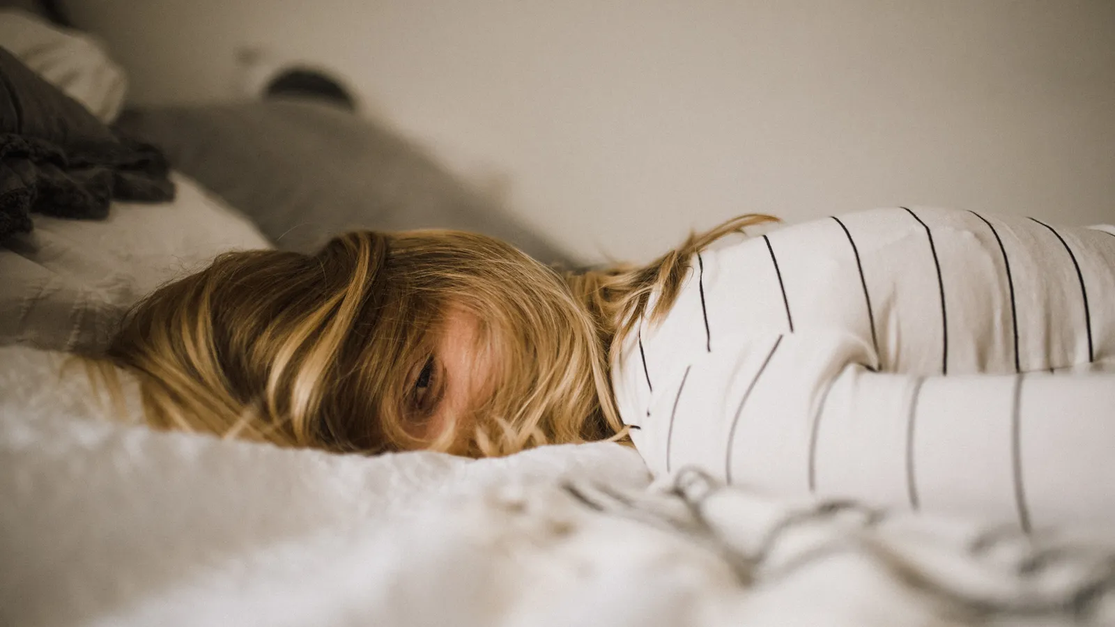 A woman lying face down across an unmade bed.