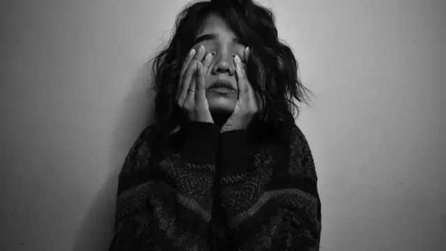 Black-and-white photo of a woman pressing her hands to her face.